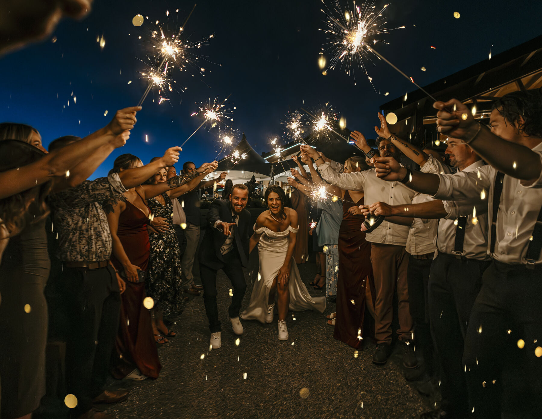 Bride and groom running through a tunnel of guests holding sparklers at night