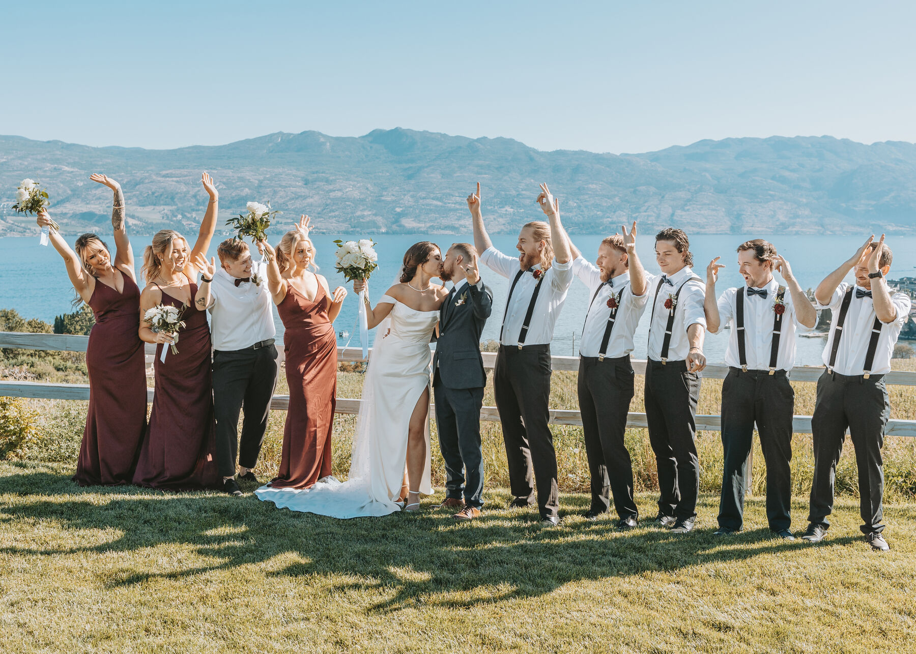 Wedding party cheering with raised arms around the bride and groom above the lake