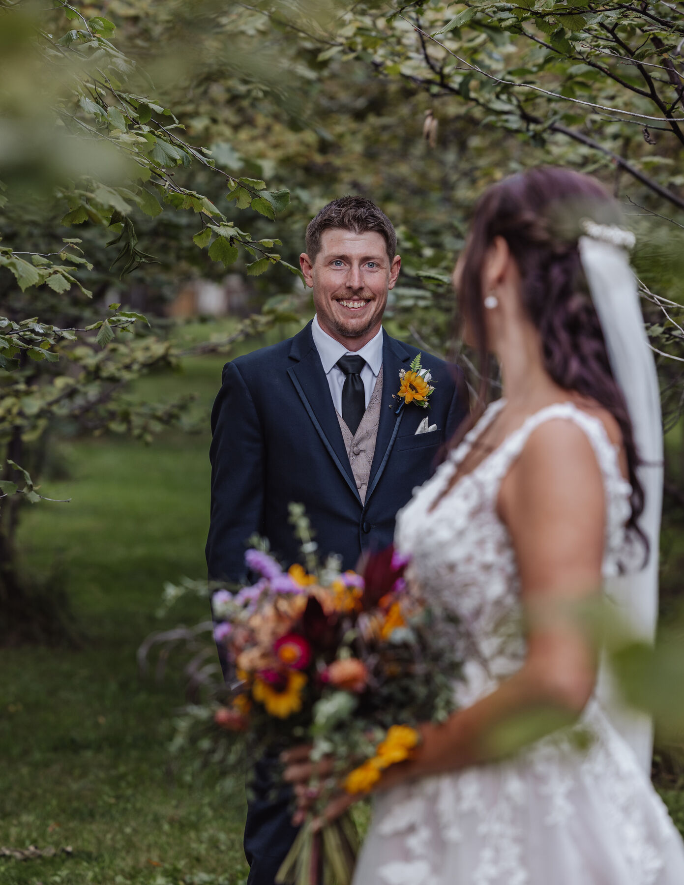 Smiling groom looking toward the camera as the bride holds a colourful bouquet