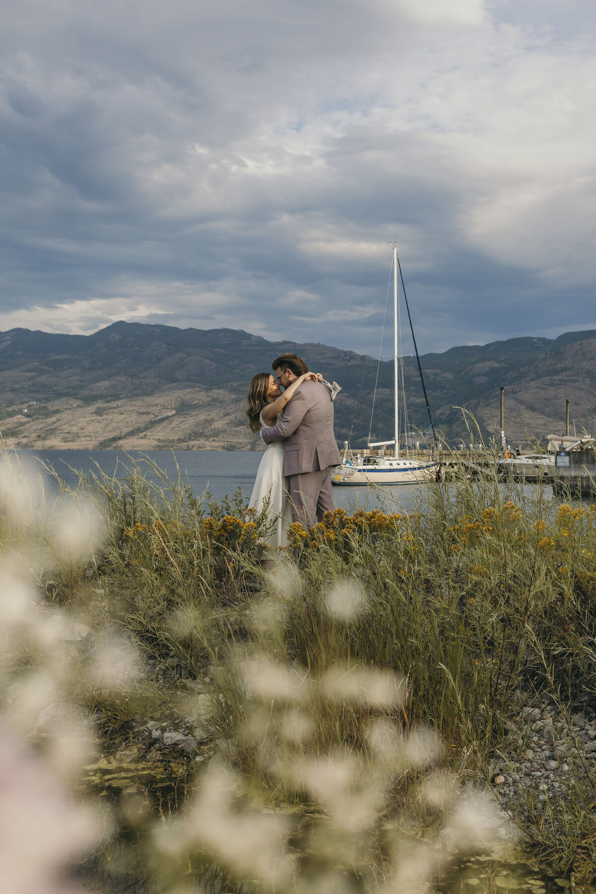 Couple kissing by the marina behind soft-focus wildflowers